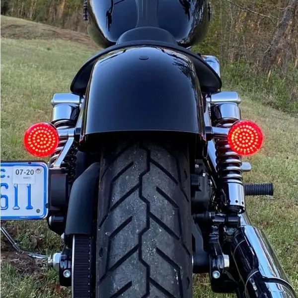 A motorcycle parked in the grass with its rear lights on.