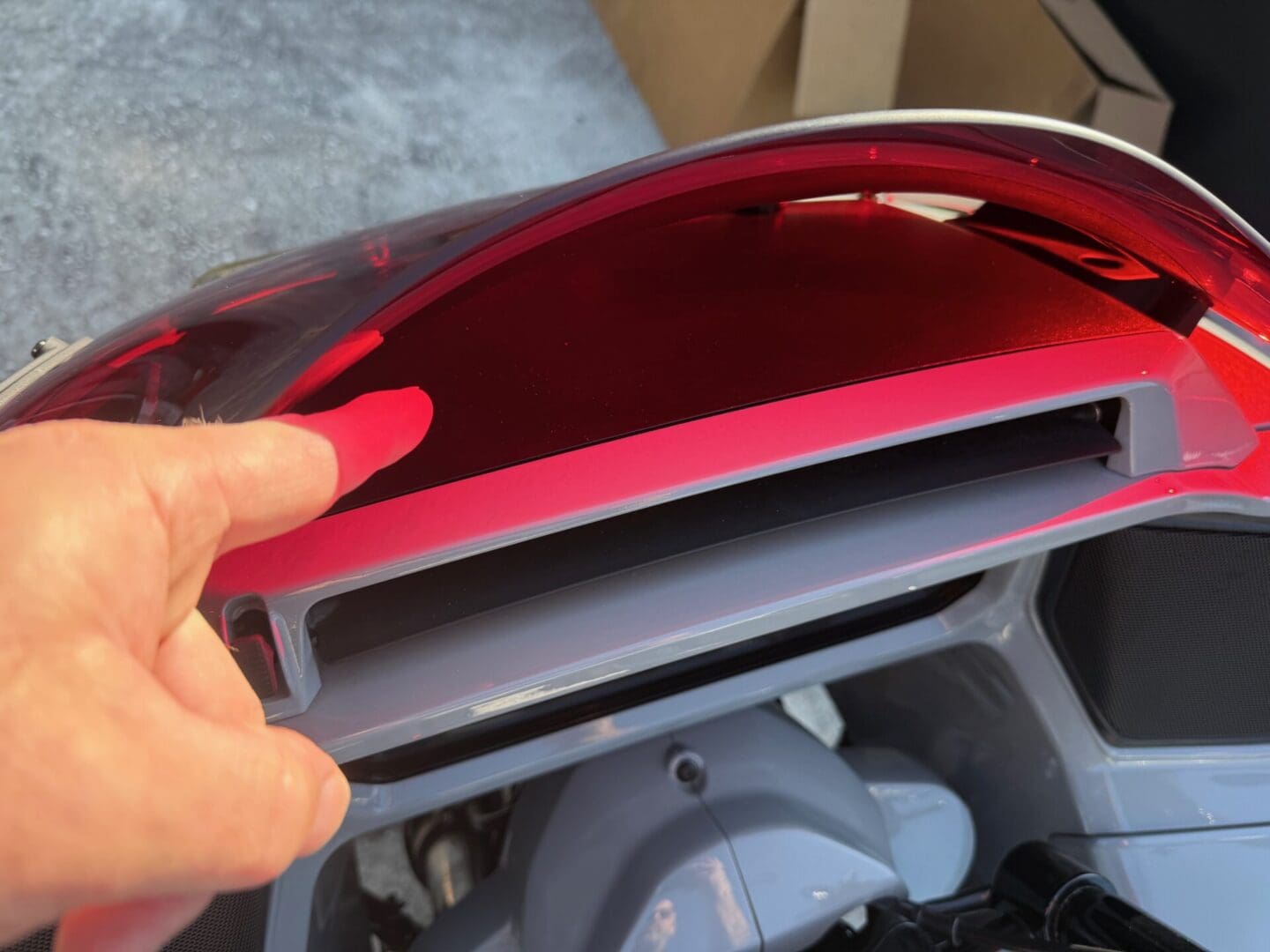 Hand touching motorcycle dashboard compartment cover.